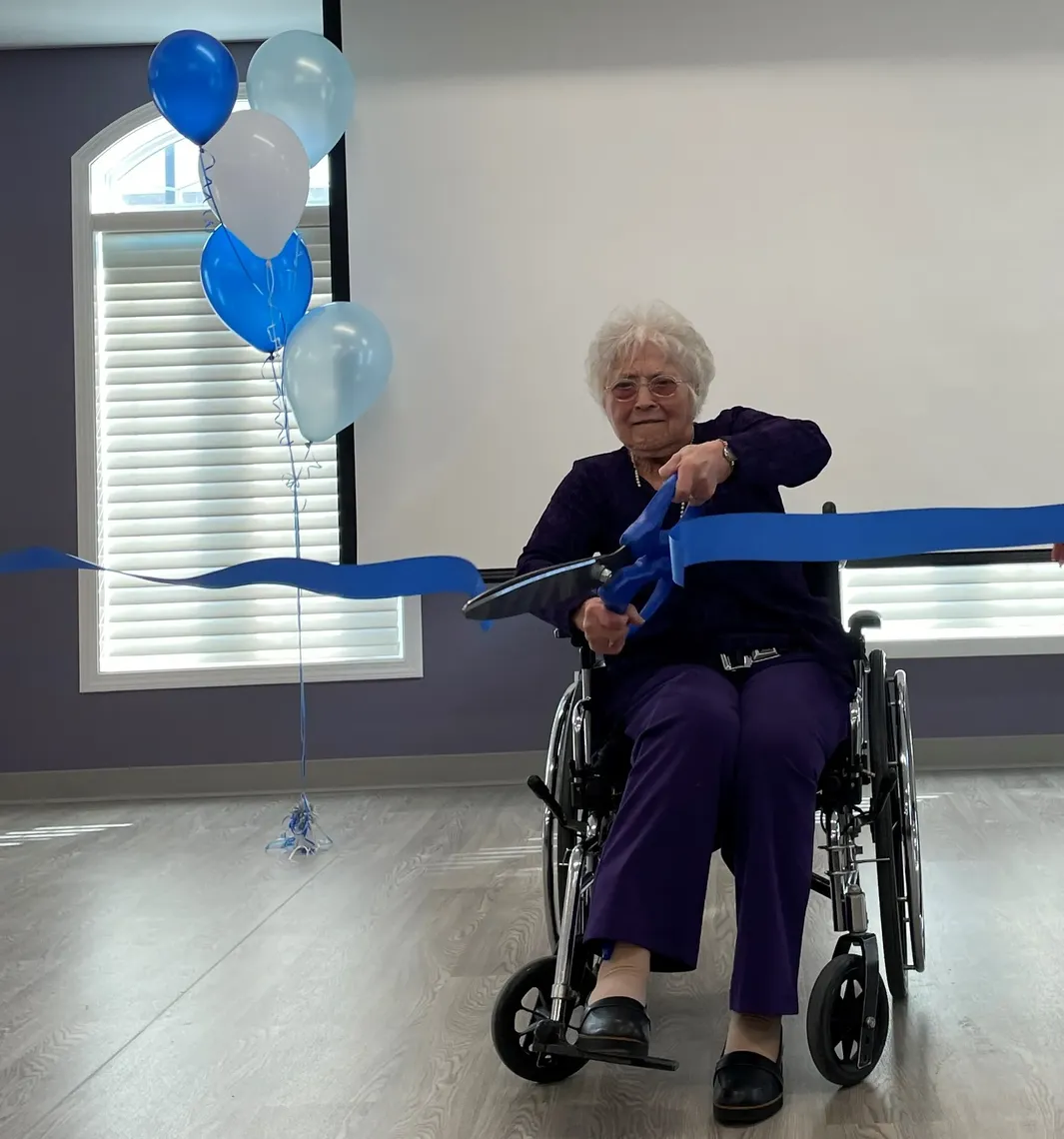 happy older woman in wheelchair cutting blue ribbon